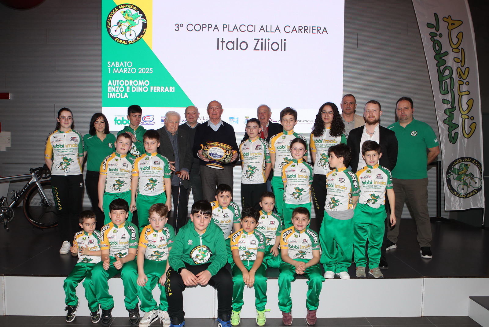 Un altro pomeriggio di ciclismo è andato in scena all’Autodromo Enzo e Dino Ferrari di Imola. Sabato 1 marzo, la presentazione della società sportiva giovanile Ciclistica Santerno Fabbi Imola, attiva dal 1995, che si presenta ai nastri di partenza del 2025 con venti giovani ciclisti dai 6 ai 14 anni, con 15 Giovanissimi e 5 Esordienti. Una occasione in cui la Ciclistica Santerno Fabbi Imola ha potuto anche celebrare tanti protagonisti dei suoi primi trent'anni, tra cui Ilario Rossi, Giocondo Fabbi, Mirko Fabbi, Valter Dosi, Andrea Dosi, Luca Martelli e tutti i volontari che contribuiscono all'attività dell'associazione. Tra gli ospiti istituzionali della giornata, il sindaco di Imola Marco Panieri, il direttore dell'Autodromo Pietro Benvenuti, il vicepresidente del comitato regionale FCI Alessandro Spada, il presidente provinciale FCI Antonio Ussia e altre personalità del mondo del ciclismo. Tra i momenti della giornata, la premiazione della 3° Coppa Placci alla Carriera a Italo Zilioli, che ha raccontato aneddoti della sua storia ciclistica, della Coppa Placci vinta nel 1973 con la maglia della Dreherforte a forti tinte imolesi, oltre a salutare la stagione agonistica di Giovanissimi ed Esordienti della Santerno Fabbi con argomentazioni ben auspicanti e frutto della propria esperienza ciclistica. A salutare la grande carriera di un importante ciclista e uomo di spessore come Italo Zilioli, anche tanti ex ciclisti professionisti, massaggiatori e ex ciclisti professionisti, massaggiatori e meccanici del team Dreherforte, tra cui Battista Babini, Gino Cavalcanti, Primo Franchini, Renato Laghi, Mauro Landini, Romano Piancastelli, Luigi Sarti e Gilberto Vendemiati. La società sportiva gialloverde, fondata dal primo presidente Ilario Rossi, seguito poi da Luca Martelli, e dal 2023 presieduta da Luca Medri, ha presentato i suoi team per la nuova stagione e lo staff che comporrà il direttivo e lo staff tecnico. È stata anche occasione per ricordare altri importanti appuntamenti organizzativi nel corso della stagione, tra cui il Gran Premio Fabbi Imola che si disputerà sabato 30 e domenica 31 agosto 2025. Il premio ricevuto da Italo Zilioli, assegnato in precedenza anche a Marino Amadori e Davide Cassani, è stato ideato dalla Santerno Fabbi insieme alla Fondazione Luciano Pezzi (l’idea viene da Fausto Pezzi, figlio di Luciano). Un premio apprezzato e validato già dalla prima edizione del 2023, nel centesimo anniversario dalla prima Coppa Placci, dai soggetti imolesi storicamente coinvolti nella corsa professionistica organizzata dall’Us Imolese, da Nino Ceroni a Virgilio Rossi e Edore Campagnoli, fino a Marco Selleri, presidente della Nuova Ciclistica Placci 2013. In sala stampa dell’Autodromo i partecipanti hanno trovato anche una mostra di bici curata da Walter Dosi e Fausto Pezzi relativa in particolare agli anni di attività del team Dreherforte.